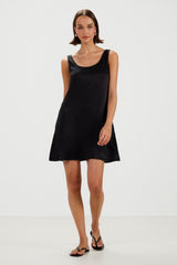 A woman modeling a black sleeveless mini dress with a scoop neckline and a flared silhouette, paired with black sandals, against a plain white studio background.